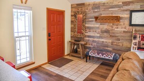 Une pièce avec un mur en bois, une porte rouge, un banc et une petite table avec une lampe.