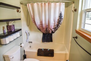 A bathroom with a bathtub, toilet, and a shower curtain. - Whispering Pines on the River (Red River)