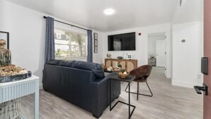 Ein modernes Wohnzimmer mit einem dunklen Sofa, einem kleinen Tisch und einem an der Wand befestigten Fernseher.