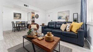 Ein modernes Wohnzimmer mit einem dunklen Sofa, einem Holztisch und einem Essbereich mit Tisch und Stühlen.