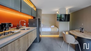 Une cuisine moderne équipée d’un réfrigérateur encastré, d’une machine à café et d’un plan de travail en bois. On y trouve également un petit coin repas avec une table et des chaises.