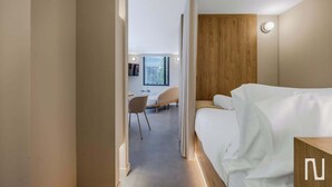 Een moderne hotelkamer met een bed, een accentmuur van hout, een bureau met stoel, en een raam dat natuurlijk licht binnenlaat.