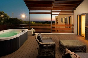 En træterrasse med jacuzzi, fletmøbler og udsigt til solnedgangen.