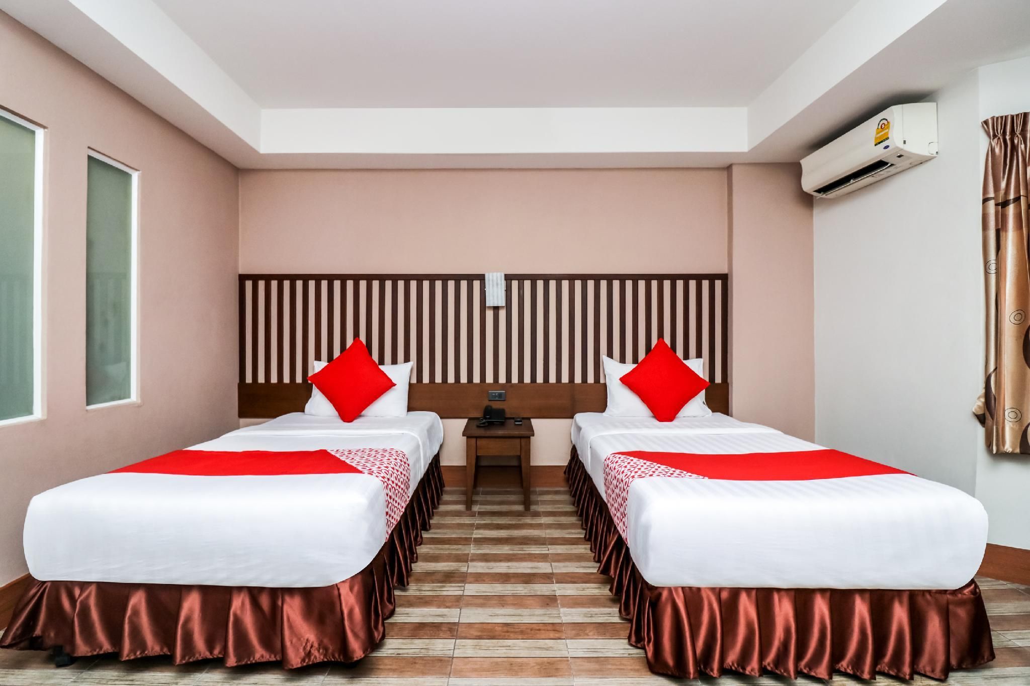 A hotel room with two beds, a headboard, a nightstand, and an air conditioning unit.