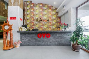 Un comptoir d'accueil avec un mur décoré d'un motif, une horloge et une plante en pot.