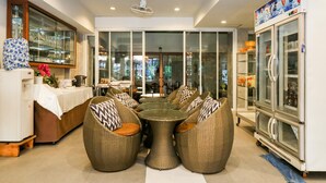 A dining area with wicker furniture, a glass door leading outside, and a refrigerator with a beverage display. - Ja Siam City (Pattaya)