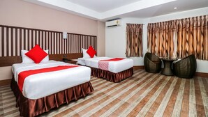 A hotel room with two beds, a wooden headboard, a small round table, and a pair of wicker chairs. - Ja Siam City (Pattaya)