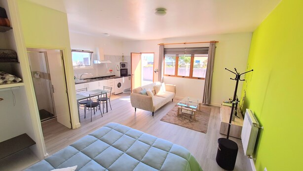 A compact living space with a kitchenette, a dining area, a sofa, and a large window. - Studio Apartment (Santana)