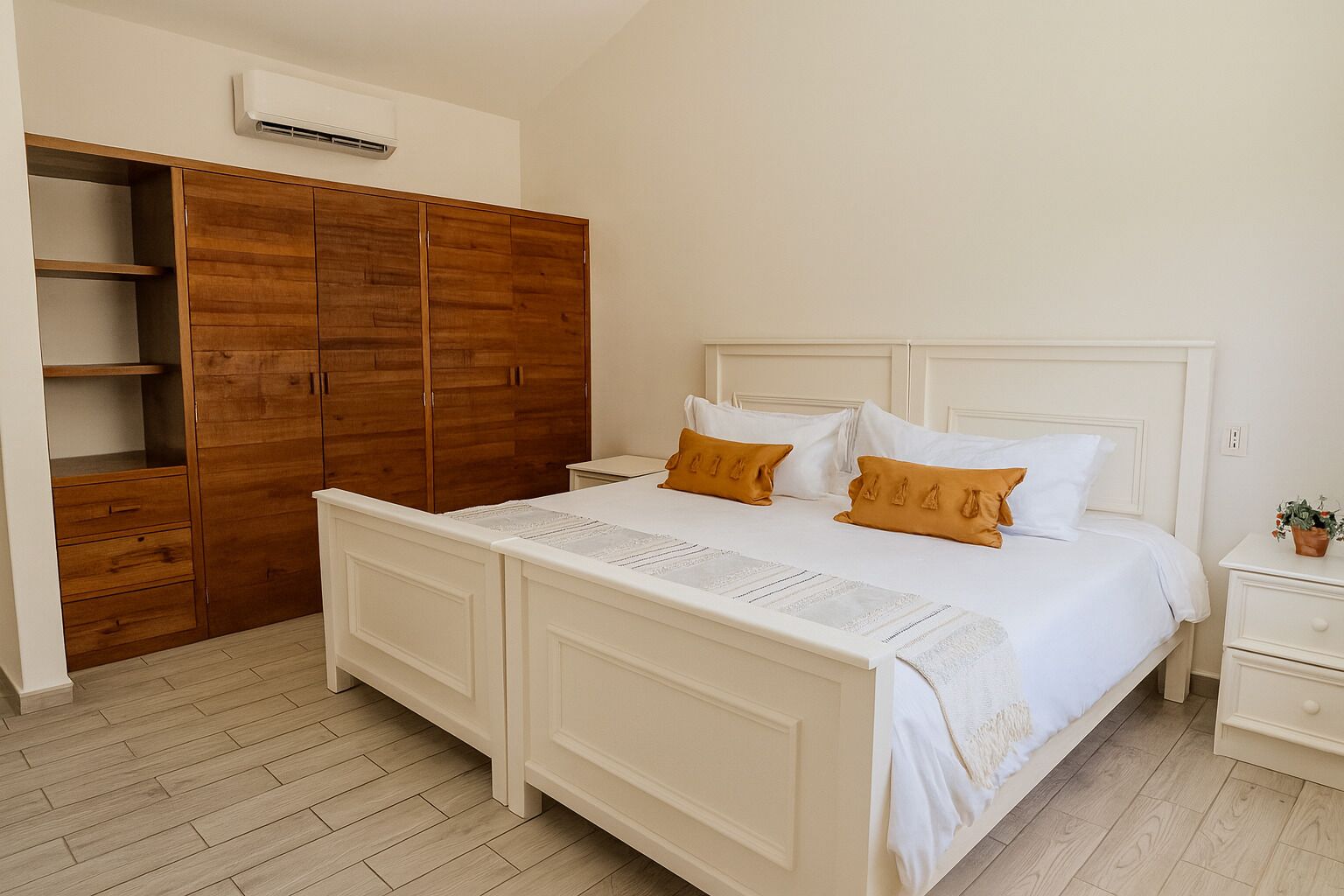 Ein Schlafzimmer mit einem Bett, weißen Nachttischen, einem Holzschrank und einer weißen Klimaanlage an der Wand.