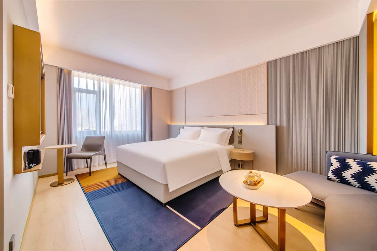 A hotel room with a bed, a chair, a small table, a sofa, and a window with curtains.
