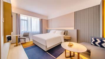 Una habitación de hotel con cama, una silla, una mesita, un sofá y una ventana con cortinas.