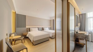 Quarto de hotel com duas camas, uma escrivaninha, uma cadeira, uma mesinha com uma chávena e um espelho.
