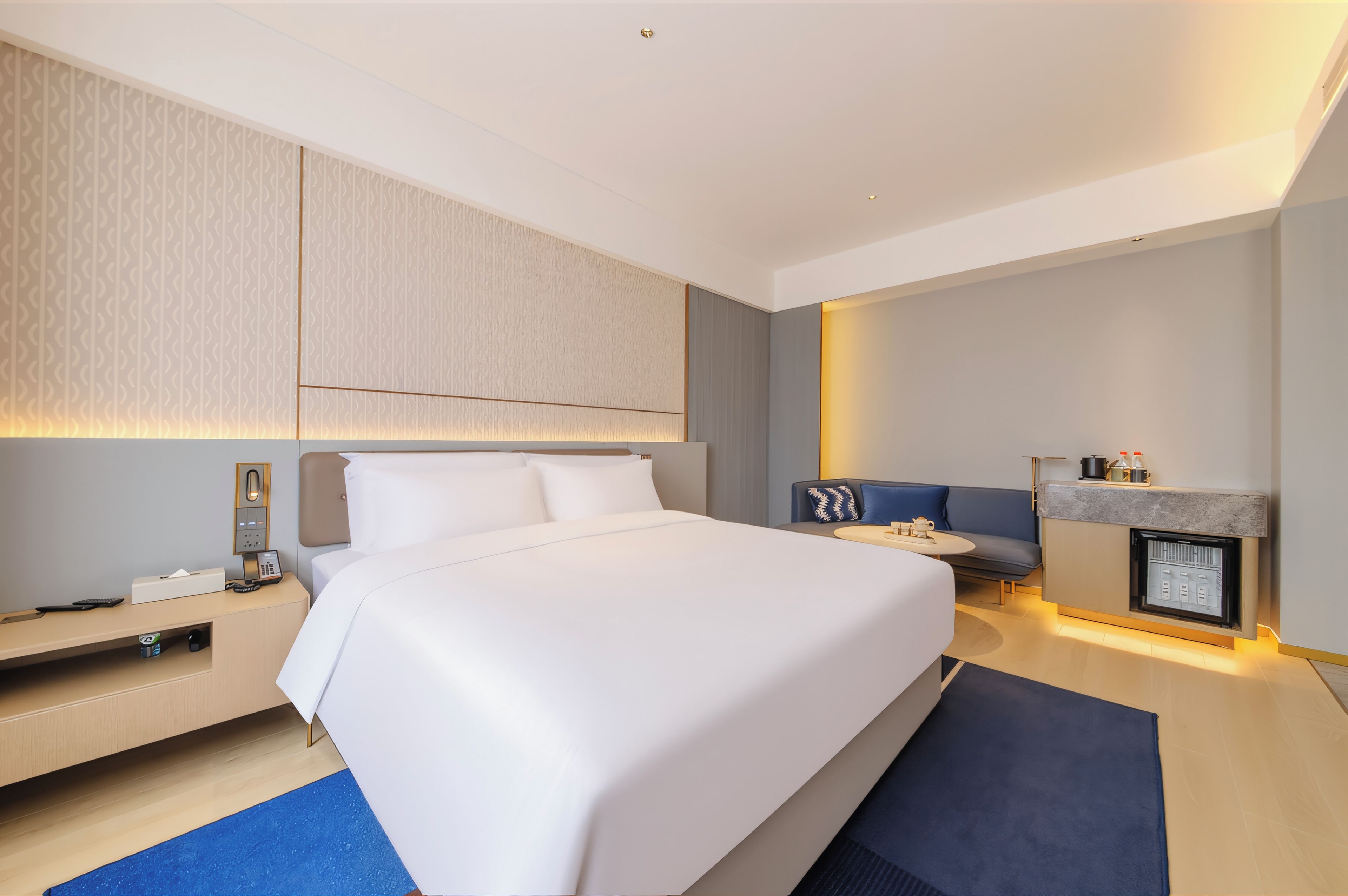 Una habitación de hotel moderna con una cama grande, un pequeño rincón de descanso, una chimenea empotrada y un mini bar.