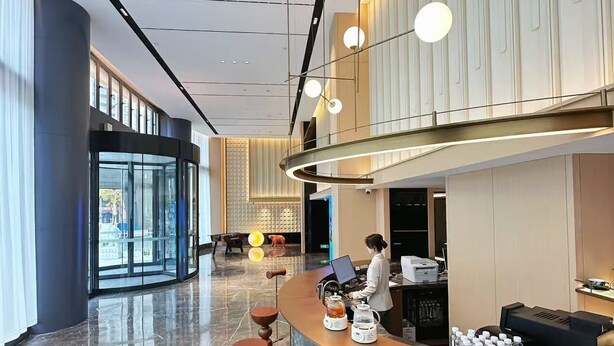 Um hall de hotel moderno com balcão de recepção, área de estar e grandes janelas.