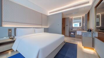 Una habitación de hotel moderna con una cama grande, un baño con tocador y espejo, y una pequeña cocina.
