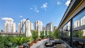 Terraço no telhado com vista para a cidade, mesas ao ar livre e plantas em vasos.