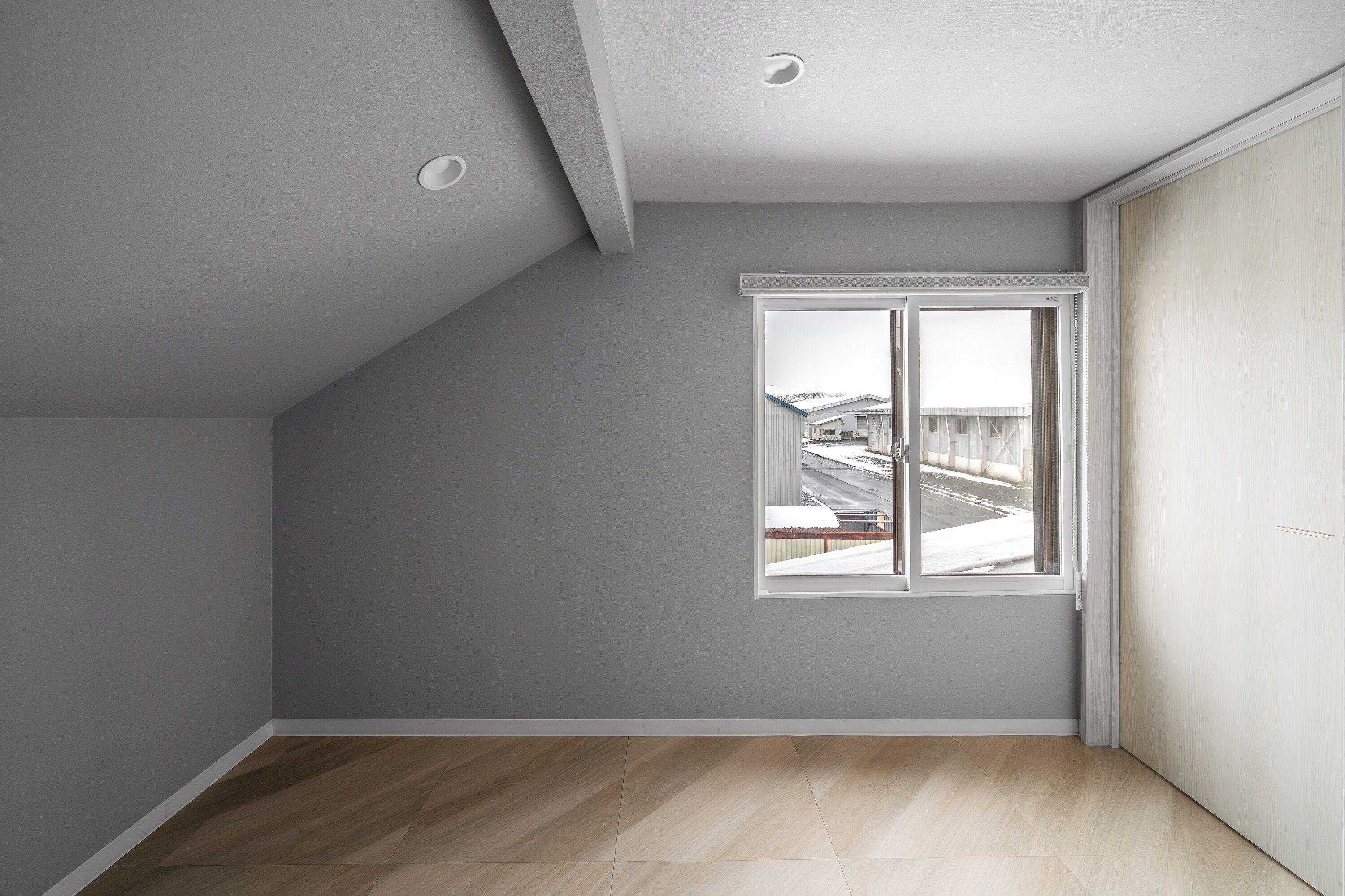 Une pièce avec un plafond en pente, une grande fenêtre donnant sur un paysage enneigé et un plancher en bois.