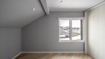 Une pièce avec un plafond en pente, une grande fenêtre donnant sur un paysage enneigé et un plancher en bois.