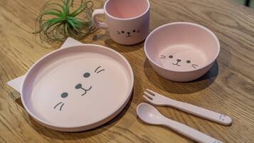 A table with a pink cat-themed plate, a pink mug, a pink bowl, and a pink spoon.