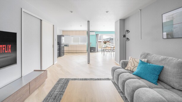 Un salon moderne avec un canapé gris, un téléviseur à écran plat et une cuisine en arrière-plan.