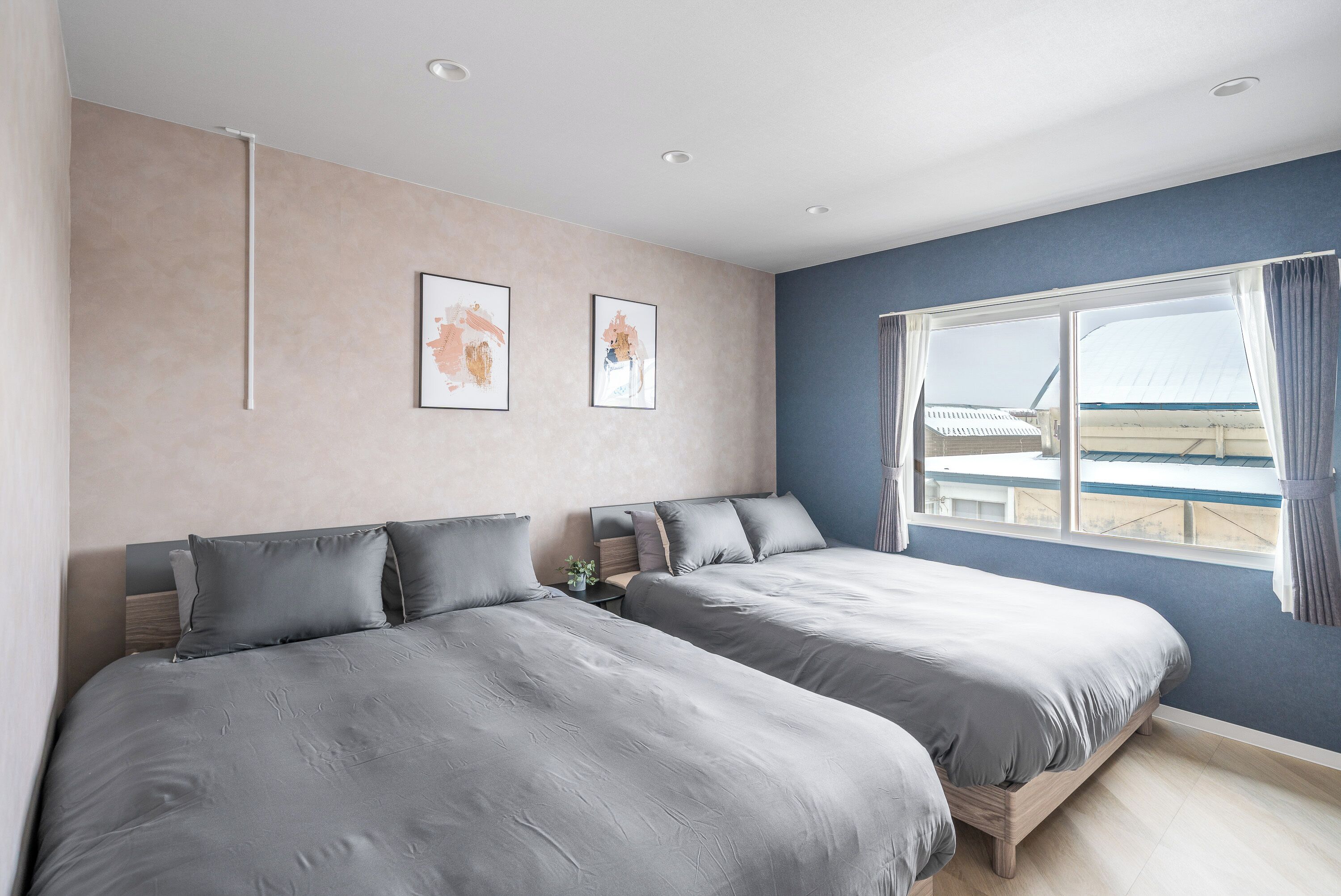 Een slaapkamer met twee bedden, een raam met gordijnen en twee kunstwerken in lijsten aan de muur.