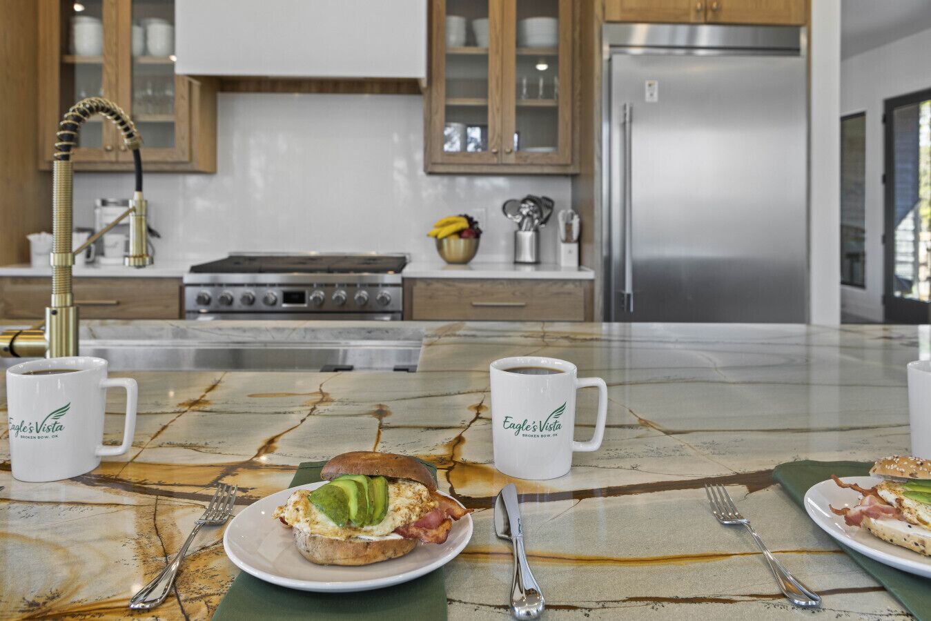 Una cocina con encimeras de mármol, un refrigerador de acero inoxidable y una estufa. Hay dos tazas blancas sobre la encimera.
