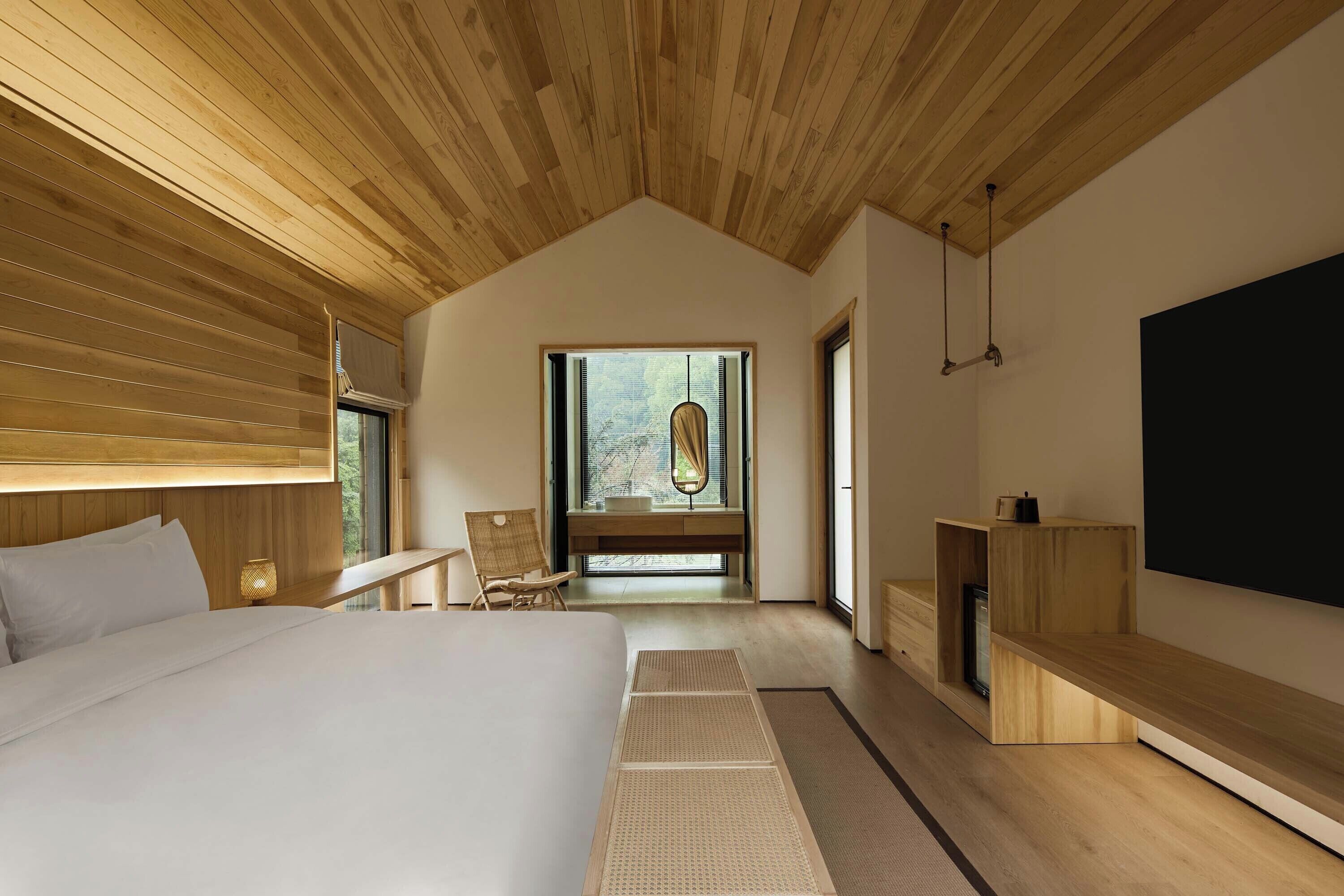 Une chambre à coucher moderne avec un grand lit, un plafond en bois, un banc intégré et un téléviseur fixé au mur.