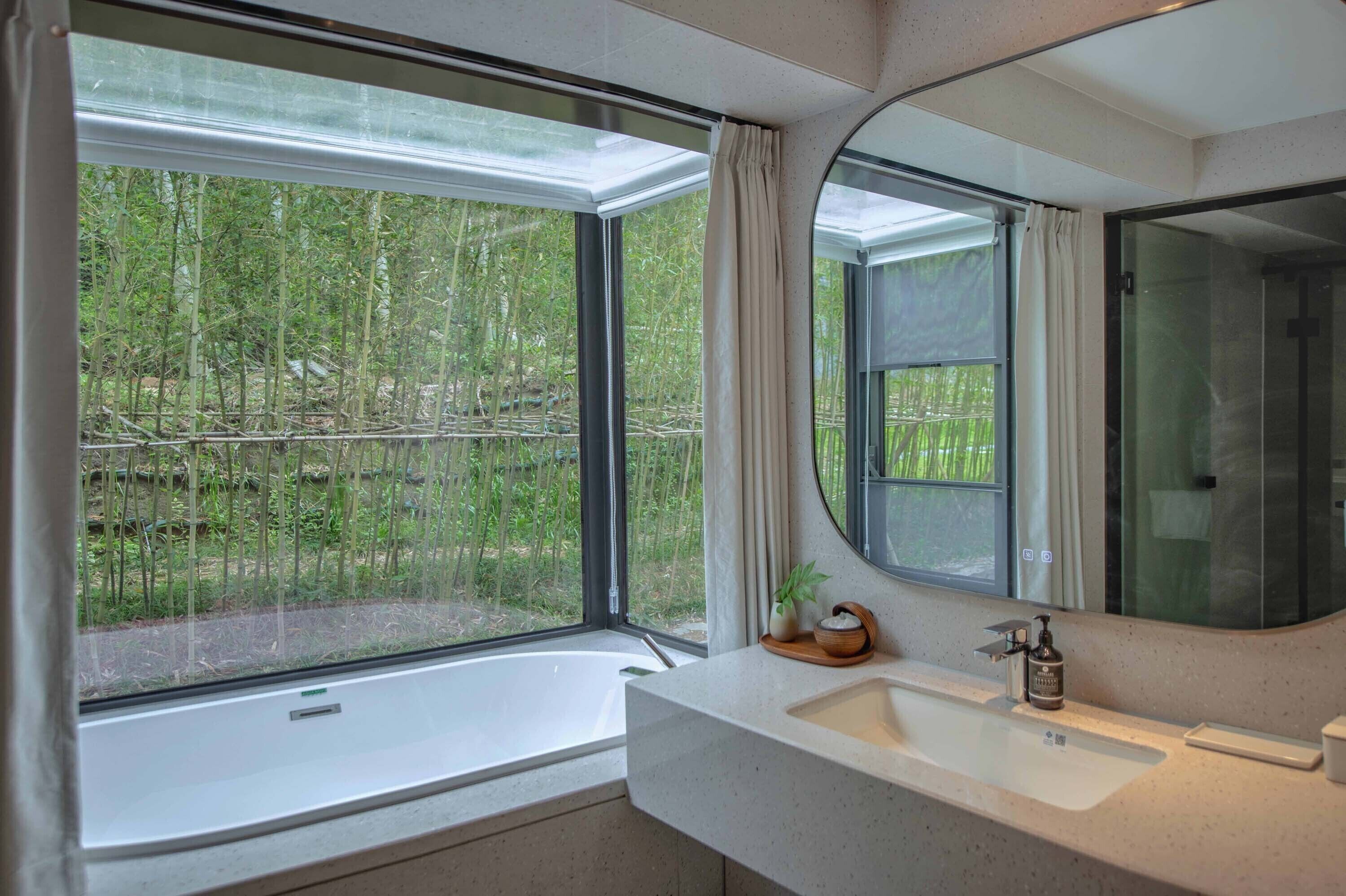 A modern bathroom with a large window, a bathtub, and a sink with a mirror.