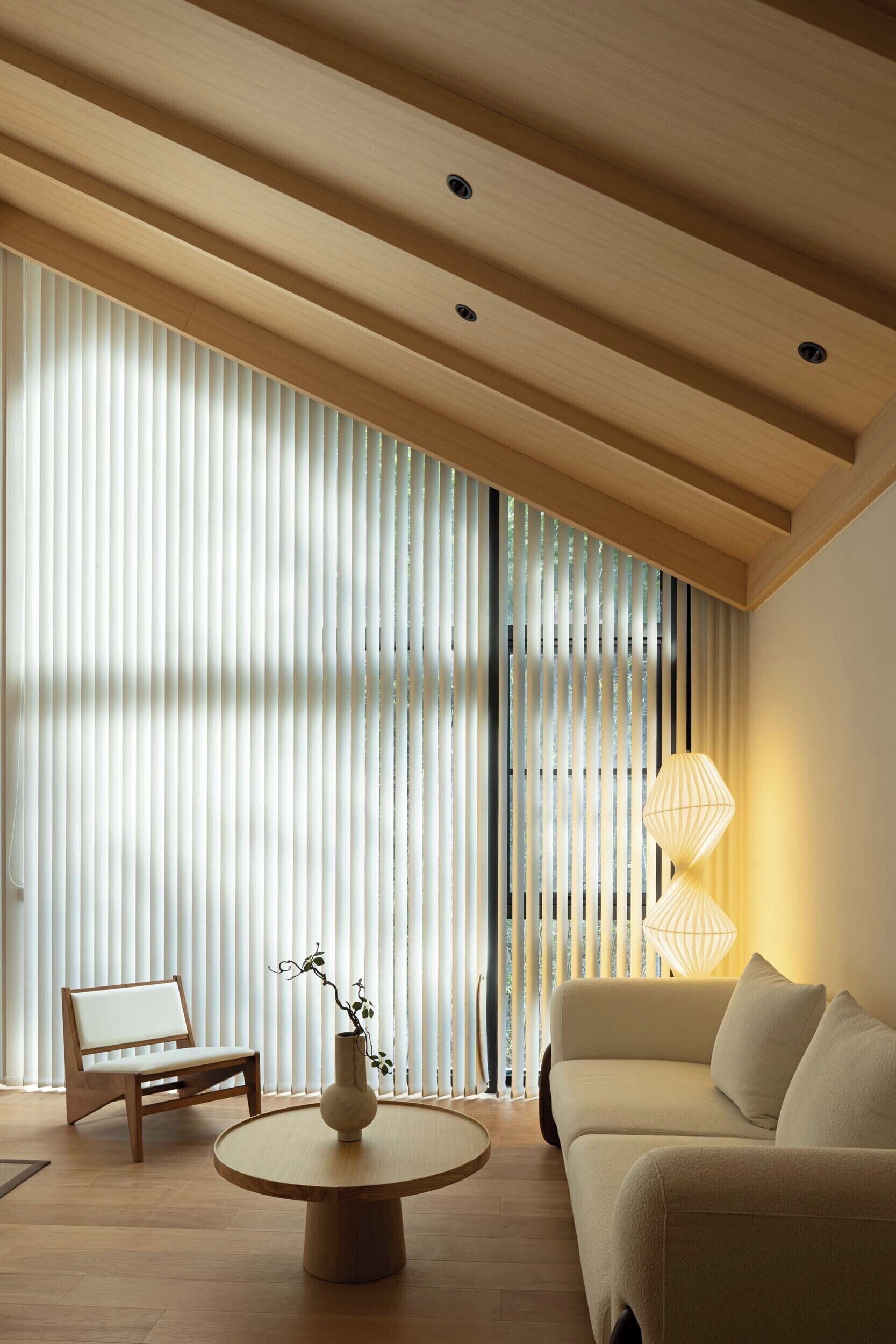 A modern living room with a wooden ceiling, a sofa, a chair, and a round table with a vase.