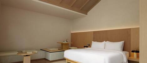 A modern bedroom with a large bed, a bedside table, a small table, and a bench.
