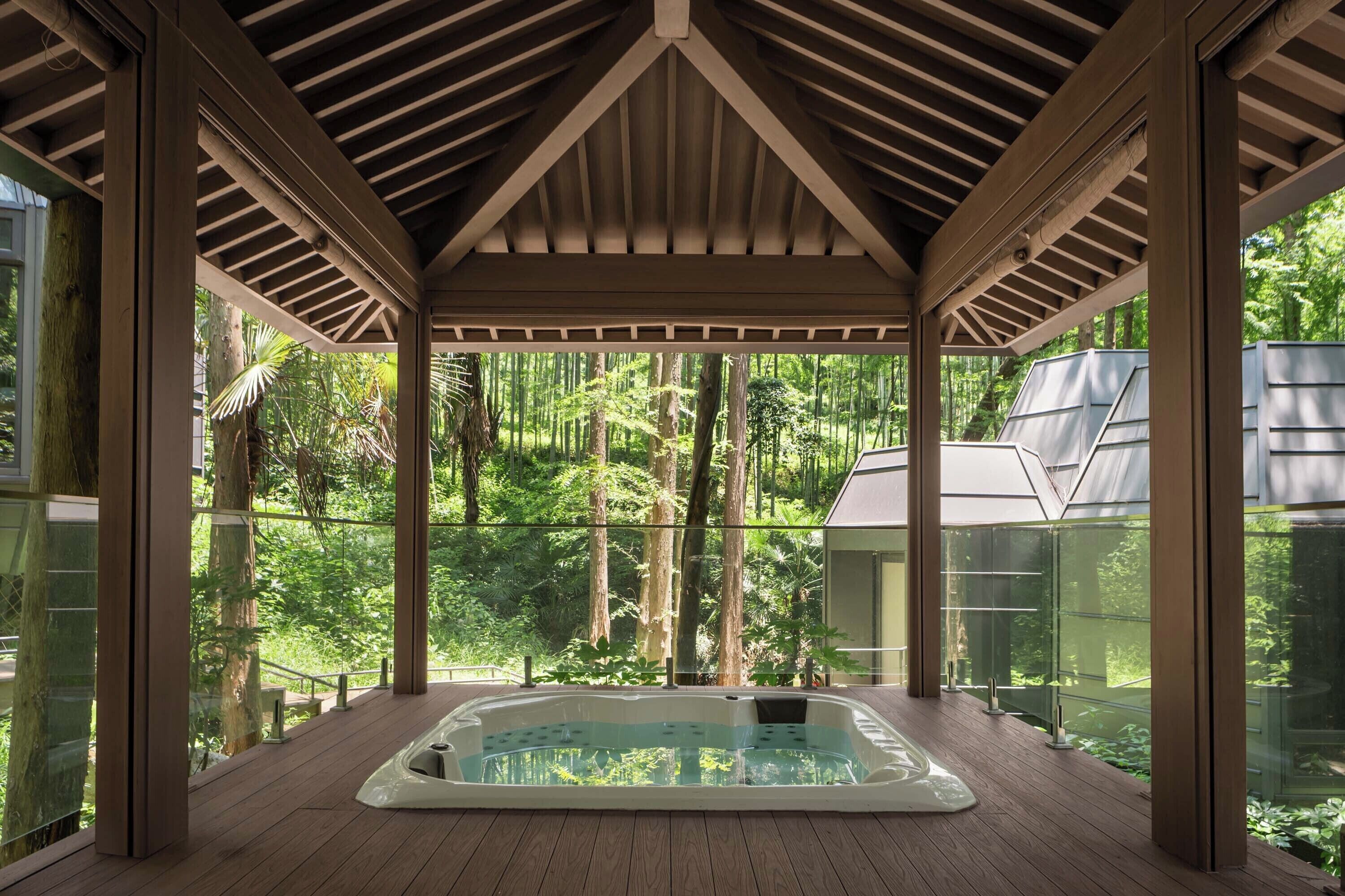 A hot tub in a wooden deck with glass walls, surrounded by a forest.