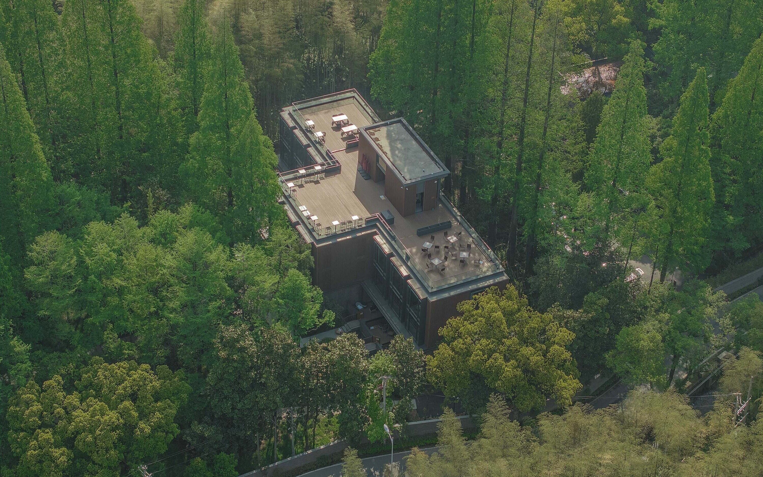 An aerial view of a modern building with a flat roof, surrounded by dense forest.