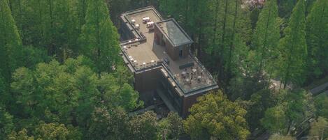 An aerial view of a modern building with a flat roof, surrounded by dense forest.