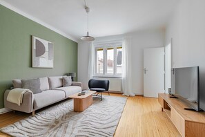 A modern living room with a sofa, armchair, coffee table, and TV stand. - Blueground | Josefstadt, view, nr Rathaus (Vienna)
