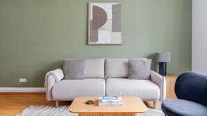 A living room with a grey sofa, patterned cushions, a wooden coffee table with books, and a modern abstract painting on the wall. - Blueground | Josefstadt, view, nr Rathaus (Vienna)