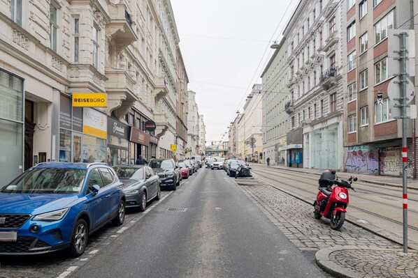 Une rue bordée de voitures garées et, sur la droite, un scooter rouge.
