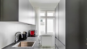 A modern kitchen with a stainless steel sink, a kettle, and a red pot on the counter. - Blueground | Josefstadt, view, nr Rathaus (Vienna)