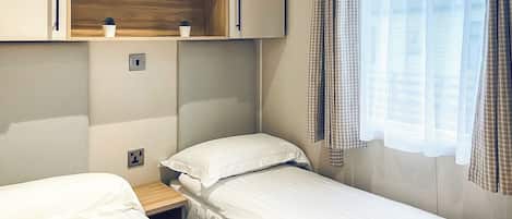 Ein Schlafzimmer mit zwei Betten, einem Holzregal mit Topfpflanzen, einem Fenster mit Vorhängen und einem Nachttisch.