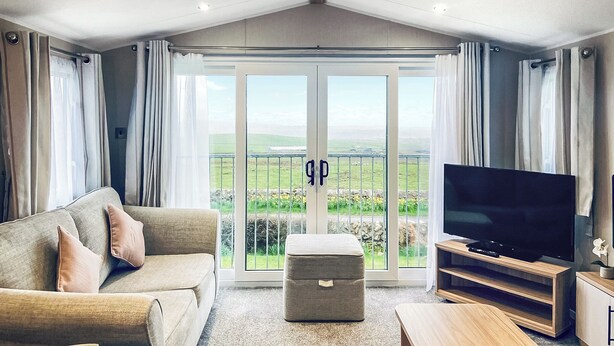 Una sala de estar moderna con sofá, reposapiés, televisor y un balcón con vistas.