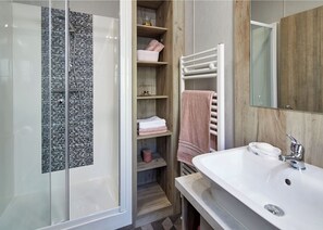 A bathroom with a glass shower enclosure, a white sink, a wooden vanity, and a towel rack.