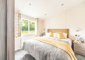 A bedroom with a large bed, a window with curtains, a bedside table, and a nightstand.