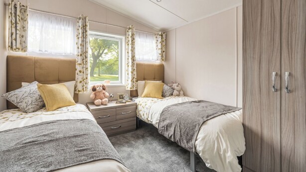 Une chambre avec deux lits, une armoire, une fenêtre avec des rideaux et un ours en peluche sur la table de chevet.