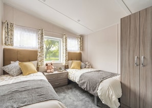 A bedroom with two beds, a wardrobe, a window with curtains, and a teddy bear on the nightstand.
