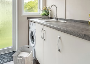 A modern kitchen with a built-in washer, a sink, and a window with a view of greenery.