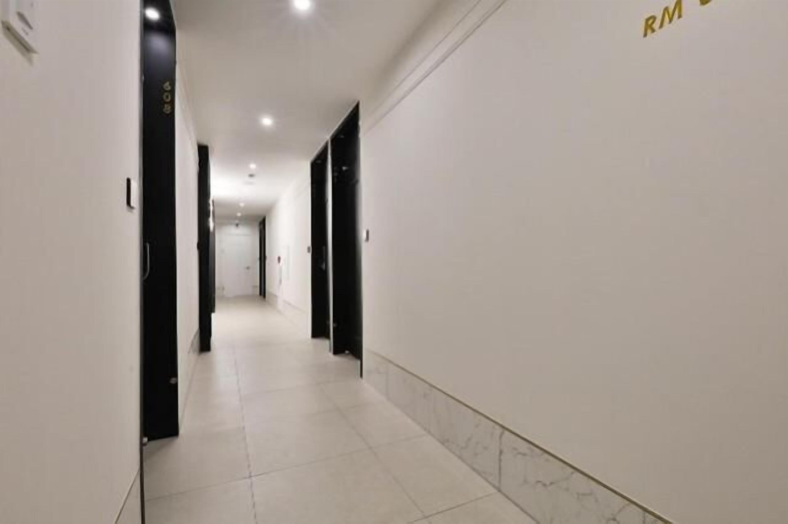 A long, narrow hallway with white walls and black doors, leading to a distant room.