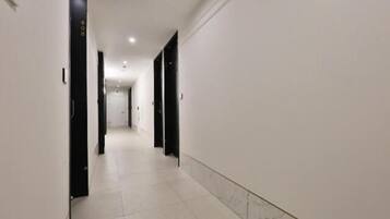 A long, narrow hallway with white walls and black doors, leading to a distant room.