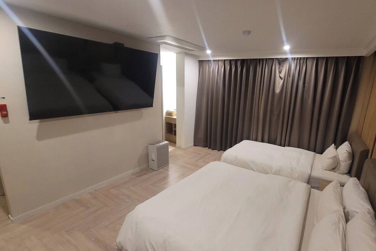 A hotel room with two beds, a TV on the wall, and a small bedside table.
