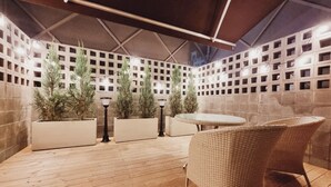 An outdoor patio with a round table and wicker chairs, surrounded by planters with tall plants and decorative lighting. - Hotel Label Seongnam (Seongnam)