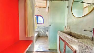 A bathroom with a red wall, a glass shower enclosure, a sink with a mirror, and a small window.