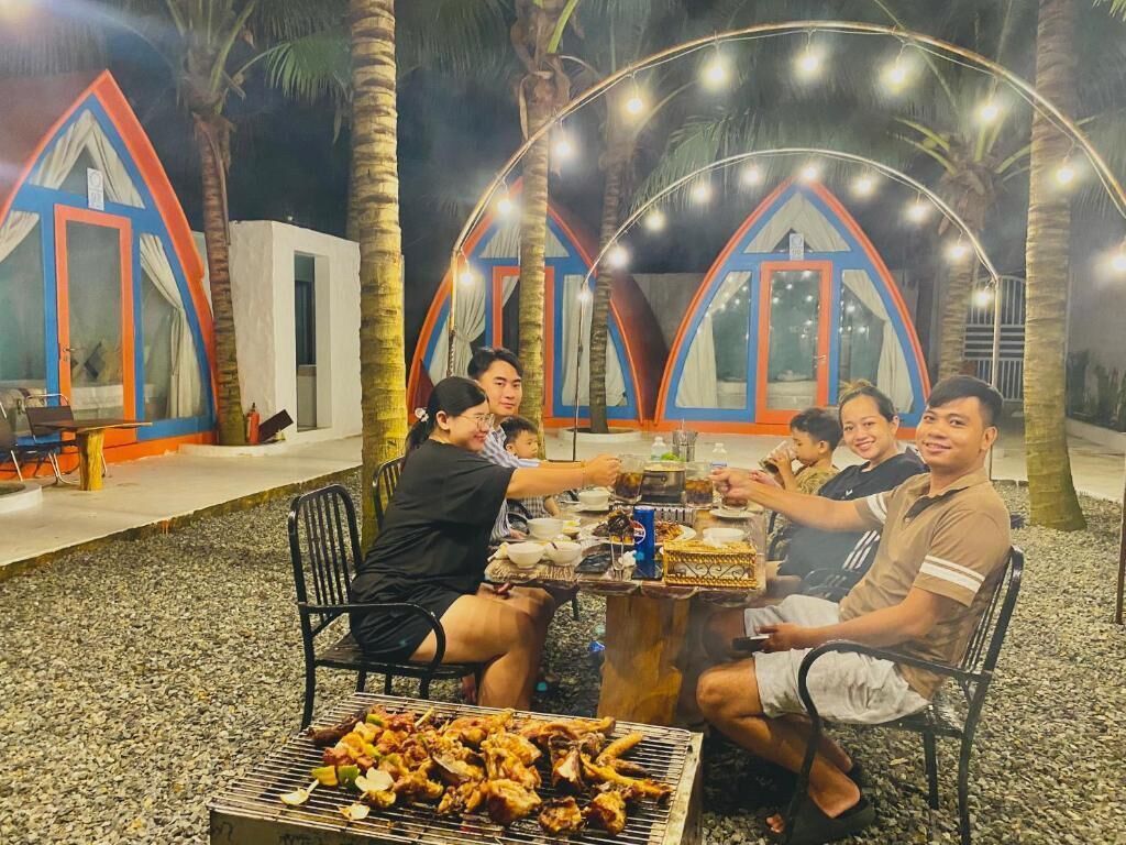 A group of people dining outdoors at a table with a grill in the foreground.